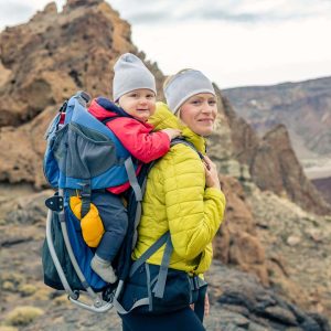 Family hike baby boy travelling in mother's backpack. Hiking adventure with child on autumn family trip in mountains. Vacations journey with infant carried on back, weekend travel in Tenerife, Spain.